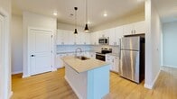 Located at 2700 Emerald Green Way in Knoxville, TN, this single-floor, 2-bedroom, 2-bathroom home offers a clean, modern design with thoughtful finishes throughout. The open-concept kitchen and living area serves as the heart of the home, showcasing crisp white cabinetry with matte black hardware, light quartz countertops, a classic subway tile backsplash, and a central island with a built-in sink and pendant lighting overhead. Stainless steel appliances — including a refrigerator, range, and microwave — complete the sleek kitchen. Light hardwood-style flooring runs throughout the main living areas, creating a bright and cohesive aesthetic. Both bedrooms are carpeted and comfortably sized, with natural light provided by windows overlooking the exterior. One bedroom features a sliding double-door closet, while the other includes a spacious walk-in closet with wire shelving for organized storage. Each bathroom is finished with light wood-style flooring, a tub/shower combo, vanity with white cabinetry, and matte black fixtures and accessories. Additional functional spaces include a dedicated laundry room, pantry, utility room, and hallway. The home's neutral palette and modern finishes lend a clean, move-in-ready feel throughout.