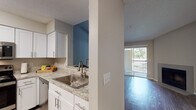 This single-story residence is characterized by an open-concept design that connects the kitchen, dining, and living areas into one cohesive space. The living area features vaulted ceilings that add a sense of height and volume, complemented by wood-style flooring throughout the main living zones. A fireplace serves as a focal point in the living room, which also benefits from natural light streaming through large sliding glass doors that open onto a private balcony with outdoor views.

The kitchen is equipped with white shaker-style cabinetry, granite-look countertops, stainless steel appliances including a range, microwave, and dishwasher, and a stainless steel sink. A pass-through window connects the kitchen to the main living area, enhancing the open feel of the space.

The bedrooms are carpeted for comfort and feature ceiling fans, natural light from windows, and access to walk-in closets with built-in shelving. The bathroom offers a wide vanity with a granite-look countertop, white cabinetry, a large mirror, and a shower-tub combination. Throughout the residence, a neutral color palette and textured ceilings contribute to a cohesive and functional aesthetic.