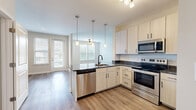 Located at 4101 Runner Lp in Chester, Virginia, this single-floor, 2-bedroom, 2-bathroom home offers a clean, modern aesthetic with thoughtful finishes throughout. The open-concept kitchen and living area serves as the heart of the home, anchored by a central island with striking granite countertops, an undermount sink with a matte black faucet, and a full suite of stainless steel appliances including a refrigerator, range, microwave, and dishwasher. Light wood-tone cabinetry with black hardware adds a contemporary touch, while pendant lighting above the island and luxury vinyl plank flooring complete the space. The living area extends naturally from the kitchen, bathed in natural light from multiple windows and sliding door access to the outdoors. Both bedrooms feature plush carpet flooring, ceiling fans, and ample natural light, with the primary bedroom offering generous proportions and dedicated closet space. The two full bathrooms are finished with granite-topped vanities and full tub-shower combinations with tiled surrounds. Neutral, warm wall tones and clean white trim flow consistently throughout the home, creating a cohesive and inviting atmosphere well-suited for comfortable everyday living.