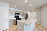 Located at 2330 Challenger Way in Watertown, South Dakota, this single-level 2-bedroom, 2-bathroom residence offers a clean, modern design with thoughtful finishes throughout. The kitchen serves as the heart of the home, showcasing a large center island with a light stone-patterned countertop and built-in sink, complemented by taupe shaker-style cabinetry, white countertops, and black appliances including a range, microwave, and refrigerator. Light-toned hardwood flooring runs throughout the main living and kitchen areas, enhancing the bright, open feel of the space. Both bedrooms are carpeted and feature windows with blinds that allow for natural light and outdoor views. The primary bedroom is generously sized with its own dedicated closet. Each of the two bathrooms features hardwood-style flooring, dark cabinetry with light countertops, and a full tub-shower combination. One bathroom includes direct access to a closet, adding practical functionality. Two closets throughout the home provide ample storage. Neutral gray-toned walls and recessed lighting throughout create a cohesive, contemporary ambiance that is both functional and inviting.