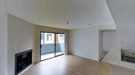 This single-floor residence offers a clean, functional layout designed to maximize comfort and usability. The main living area is bright and open, featuring light hardwood-style flooring that extends throughout the space, creating a warm and cohesive aesthetic. A fireplace anchors one side of the living room, providing both a practical heating element and a natural focal point for the room.

Large sliding glass doors lead directly to a private balcony, allowing natural light to filter into the living area and offering a seamless connection between indoor and outdoor spaces. The balcony overlooks the surrounding building exterior, providing an outdoor retreat within the unit.

The textured popcorn ceiling adds a classic residential character, while the smooth, neutral-toned walls offer a versatile backdrop suitable for a variety of interior styles. A doorway visible from the main living space leads to additional rooms, suggesting a practical flow throughout the floor plan. The overall ambiance is clean, understated, and move-in ready, making it well-suited for those seeking a straightforward and comfortable living environment.