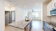 Located at 3812 W Montague Ave in North Charleston, SC, this well-appointed one-bedroom, one-bathroom unit offers a thoughtfully designed single-floor layout with a clean, modern aesthetic throughout. Light wood-tone flooring flows seamlessly across the entire space, complementing the crisp white walls and creating a bright, cohesive feel.

The open-concept kitchen is a standout feature, showcasing a center island with striking granite countertops, an undermount sink with a matte black faucet, and a bold two-tone cabinetry design combining navy blue lower cabinets with white upper cabinets. A hexagonal tile backsplash and stainless steel appliances — including a French door refrigerator, range, and microwave — complete the modern culinary space.

The kitchen flows directly into the living area, which is bathed in natural light from large windows and equipped with a ceiling fan. The bedroom offers a comfortable footprint, its own ceiling fan, and a generous window with exterior views.

The bathroom features a navy vanity with granite countertops, a framed mirror, and matte black fixtures, with direct access to a spacious walk-in closet equipped with wire shelving. A dedicated laundry room houses a full-size washer and dryer with additional overhead storage, adding everyday convenience to this efficiently designed home.