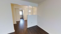 This single-floor residence offers a clean, well-maintained interior defined by rich, dark hardwood flooring that runs throughout the open living areas, creating a warm and grounded aesthetic. A standout architectural feature is the half-wall room divider framed by decorative white columns, which subtly separates spaces while preserving an open, airy feel. A delicate pendant light hangs from this divider, adding a charming focal point to the layout. The walls are finished in soft, neutral tones that complement the dark flooring and contribute to the home's bright, welcoming ambiance. Natural light filters in through a front-facing door with a window, illuminating the entryway and adjacent living areas. The layout flows naturally from one area to the next, offering a sense of connected, functional space. The textured ceiling adds a layer of subtle detail to the interior finish. Overall, the home presents a cohesive design with thoughtful architectural touches, combining classic decorative elements with practical, open-plan living in a tidy and move-in ready condition.