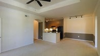 This single-floor residence showcases an open-concept layout that seamlessly connects the living area and kitchen, creating a functional and cohesive living environment. The living area features a distinctive tray ceiling accented by crown molding and a ceiling fan, adding architectural depth to the space. Neutral-toned carpet covers the floor, contributing to a warm and comfortable atmosphere.

The kitchen is thoughtfully designed with a peninsula that provides additional counter space and serves as a natural divider between the cooking and living areas. Dark countertops contrast with the white peninsula base, while warm wood-toned cabinetry lines the kitchen walls. Black appliances, including a refrigerator and range, complement the overall color scheme. Track lighting illuminates both the kitchen and an adjacent dining area, ensuring ample task and ambient lighting throughout.

A graceful arched doorway leads from the main living space to additional areas of the home, adding a classic architectural touch. Two-tone wall treatment in the dining area, with a darker lower half, provides visual interest and definition. Overall, the space offers a practical and stylish layout suited for everyday living.