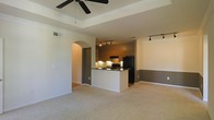 This single-floor residence showcases an open-concept layout that seamlessly connects the living area and kitchen, creating a functional and cohesive living environment. The living area features a distinctive tray ceiling accented by crown molding and a ceiling fan, adding architectural depth to the space. Neutral-toned carpet covers the floor, contributing to a warm and comfortable atmosphere.

The kitchen is thoughtfully designed with a peninsula that provides additional counter space and serves as a natural divider between the cooking and living areas. Dark countertops contrast with the white peninsula base, while warm wood-toned cabinetry lines the kitchen walls. Black appliances, including a refrigerator and range, complement the overall color scheme. Track lighting illuminates both the kitchen and an adjacent dining area, ensuring ample task and ambient lighting throughout.

A graceful arched doorway leads from the main living space to additional areas of the home, adding a classic architectural touch. Two-tone wall treatment in the dining area, with a darker lower half, provides visual interest and definition. Overall, the space offers a practical and stylish layout suited for everyday living.