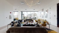 This thoughtfully designed single-floor amenity space offers a diverse range of social and recreational environments, each with a distinct character and purpose. The centerpiece is a generous lounge area bathed in natural light from expansive floor-to-ceiling windows, providing panoramic urban views. The lounge is elegantly furnished with plush sofas and armchairs in rich mustard, charcoal, and neutral tones, anchored by a bold sculptural chandelier that curves gracefully across the white ceiling. Warm hardwood flooring and layered area rugs add texture and definition to the open layout. A dedicated games room, finished with vibrant blue flooring, houses a full-size pool table and a ping-pong table, all set against a backdrop of uninterrupted city views through wraparound glazing. A compact, well-appointed wet bar with white subway tile, open shelving, and under-counter refrigeration supports the entertaining spaces. A moody screening and event room features deep charcoal walls with cove lighting, rich terracotta carpeting, and a generous wraparound banquette, lending an intimate atmosphere for gatherings or performances. An additional lounge nook offers low-profile seating in warm rust tones positioned directly against full-height windows with striking cityscape views, creating a comfortable retreat within the overall space.