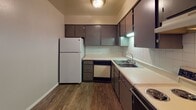 Located at 6500 St Joe Rd in Fort Wayne, Indiana, this single-floor unit offers a practical and comfortable layout designed for everyday living. The kitchen is efficiently arranged in a U-shaped configuration, featuring dark-toned cabinetry with ample upper and lower storage, white laminate countertops, a white tile backsplash, a double-basin sink, and full appliance package including a refrigerator, dishwasher, and range. Durable wood-look flooring runs throughout the kitchen, adding a warm contrast to the neutral cabinetry. The full bathroom continues the wood-look flooring and includes a vanity with matching dark cabinetry, a well-lit mirror, tile accent wall, and a full tub-shower combination. The bedroom is generously proportioned with soft carpeting and a large window that welcomes natural light and outdoor views. The spacious living area is carpeted and features a ceiling fan, neutral wall tones, and a sliding glass door that opens to an outdoor space, filling the room with natural light. The overall layout flows efficiently from the entry through the living space and into the kitchen and private rooms, creating a cohesive and functional living environment.