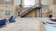 Located at 821 W Lake St in Fort Collins, Colorado, this generously sized outdoor amenity courtyard is nestled within a multi-story residential building, creating a private, enclosed retreat for its residents. The space is defined by striking natural stacked-stone walls in warm cream and golden tones, which wrap around the courtyard and lend a refined, resort-like aesthetic throughout.

At the heart of the space is a freeform swimming pool with a tanning ledge, complemented by an adjacent raised hot tub — both finished in crisp aqua blue tile. A row of lounge chairs lines the pool deck, offering ample space for sunbathing and relaxation. Nearby, a covered outdoor pavilion with a metal standing-seam roof houses a built-in grill and kitchen area, while a fire pit surrounded by Adirondack-style seating provides a welcoming social gathering spot.

The concrete patio deck is expansive and well-maintained, connecting all amenity zones seamlessly. Steel stairways with black metal railings provide elevated access to upper-level walkways and balconies that overlook the courtyard. Restroom facilities are conveniently accessible directly from the courtyard. The surrounding multi-story building architecture, with its mix of siding, brick, and stone, frames the space and enhances its sense of enclosure and community.