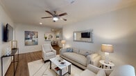 This single-story residence in Baton Rouge, Louisiana, presents a cohesive and comfortable layout across two bedrooms and two bathrooms. The open-concept living area serves as the heart of the home, featuring wood-look flooring, crown molding, and a ceiling fan overhead. Natural light filters through windows dressed with curtain panels, lending a warm, inviting atmosphere. The space flows naturally toward a dining area, creating a functional and connected common area.

The kitchen is equipped with rich, dark-stained cabinetry, light granite-style countertops, and stainless steel appliances, including a refrigerator and dishwasher. Track lighting overhead and wood-look flooring complete the functional yet stylish workspace.

Both bedrooms are generously proportioned, each featuring plush carpeting, ceiling fans, and windows with blinds and curtain panels that allow for ample natural light. The neutral color palette and soft tones throughout contribute to a restful ambiance in each room.

The bathrooms are finished with dark wood cabinetry paired with granite-style countertops. One bathroom features a tub-shower combination with a curved curtain rod, tile flooring, and well-organized storage above. The overall design of this residence balances practicality with a clean, contemporary aesthetic.
