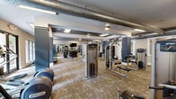 Located at 131 Poindexter Drive in Charlotte's South End neighborhood, this well-appointed fitness center offers a comprehensive workout facility spread across a single, generously sized floor. The space is divided into two primary zones connected by hallways, each thoughtfully designed to serve distinct exercise needs.

The main exercise room features a modern, open layout with high ceilings and exposed ductwork that lends an industrial-chic character to the space. Neutral-toned carpet flooring, recessed and flush-mounted lighting, and floor-to-ceiling windows bring in abundant natural light while providing views of the surrounding greenery. The room is outfitted with a full array of Precor strength machines, cable systems, free weights including a complete dumbbell rack, and cardio equipment such as treadmills and ellipticals. Large wall-mounted mirrors and a flat-screen TV enhance the experience throughout.

A dedicated studio room adjoins the main gym and features warm hardwood flooring, bold blue accent walls, and oversized windows that flood the space with natural light. This area is equipped with indoor cycling bikes, rowing machines, TRX suspension trainers, kettlebells, medicine balls, and stability balls, making it ideal for group classes or independent functional training. A large wall mirror and mounted flat-screen display complete the studio setup, creating a versatile and motivating environment for all fitness levels.