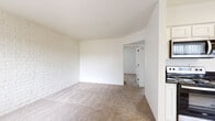 Located at 1250 E Tenth St in Tucson, Arizona, this single-floor unit showcases a distinctive character defined by white-painted exposed brick walls that carry throughout the space, creating a bright and cohesive aesthetic. The living area is generously proportioned, featuring neutral carpet flooring and a clean, open layout that flows seamlessly into adjoining rooms. The kitchen stands out with its modern updates, including white shaker-style cabinetry, dark countertops, stainless steel appliances — including a refrigerator, range, microwave, and dishwasher — and light wood-look vinyl flooring. A skylight adds an additional source of natural light to the kitchen. The bedroom offers comfortable carpeted flooring, white brick accent walls, a window with vertical blinds for natural light, and a wall-unit air conditioner. A sliding-door closet provides practical storage. The bathroom is well-appointed with a full tub and shower combo, a vanity with dark countertop, and matching light wood-look vinyl flooring. Throughout the unit, the consistent use of white tones on both the walls and brick surfaces lends a clean, airy ambiance well-suited to the Tucson climate.