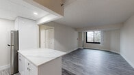This 2-bedroom, 2-bathroom residence offers a thoughtfully designed single-floor layout with contemporary finishes throughout. The open-concept kitchen and living area serves as the heart of the home, featuring a striking marble-look quartz waterfall island, crisp white cabinetry extending to the ceiling, stainless steel appliances including a refrigerator, range, microwave, and dishwasher, and recessed lighting set within a drop ceiling. The kitchen flows seamlessly into the living area, which is finished with durable grey wood-look flooring found consistently throughout the unit.

Both bedrooms are generously sized, with the primary bedroom offering ample room for a full furniture arrangement. Each bedroom features large black-framed windows that fill the spaces with natural light and frame views of the surrounding neighbourhood and greenery. The neutral white walls and clean baseboards lend a bright, move-in-ready aesthetic.

The two bathrooms are cleanly finished, with one showcasing a full soaker tub and shower combination accented by white subway tile and stylish dark hexagonal floor tile. Two hallways and a dedicated closet provide practical storage and smooth circulation throughout the unit, completing this well-organized and modern living space.