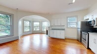 This well-appointed single-floor residence combines classic architectural character with modern updates throughout. Rich, warm hardwood floors flow seamlessly through every room, anchoring the space in timeless style. A defining feature of the layout is the elegant arched doorway that connects the living and common areas, lending a sense of graceful, open flow between spaces.

The living area is highlighted by a curved bay window that floods the room with natural light and frames pleasant outdoor views of mature trees and the surrounding neighborhood. A classic fireplace serves as a focal point, adding warmth and architectural charm. The kitchen is fully updated with crisp white shaker-style cabinetry, granite-look countertops, and a full suite of stainless steel appliances including a refrigerator, range, microwave, and dishwasher — all set atop the same gleaming hardwood floors.

Bedrooms are generously sized, with large windows offering natural light and neighborhood views, and include ceiling fans and closet storage. The bathroom features neutral stone-look tile flooring and a window for natural ventilation. Throughout the unit, clean white walls, gray trim accents, and abundant natural light from multiple windows create a bright, airy atmosphere that is both inviting and functional.