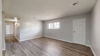 This single-story space presents a clean, neutral aesthetic throughout, united by consistent wood-look plank flooring and light gray walls with crisp white baseboards. The layout, as revealed by the floor plan view, includes multiple rooms arranged around a central corridor, offering a functional and well-organized flow.

The main living area is generously sized, featuring a textured ceiling, a ceiling-mounted HVAC vent, and a window with blinds that admits natural light. A dedicated door provides additional access or storage connectivity within this space.

The secondary rooms maintain the same neutral palette and flooring, each equipped with windows fitted with blinds for light control and privacy. These rooms offer versatile usage options and include multiple electrical outlets along the walls.

The galley-style kitchen stands out with its bright white cabinetry, granite-look countertops, a stainless steel sink, and a full suite of white appliances including a coil-top range and refrigerator. A skylight panel overhead enhances the brightness of this workspace considerably.

Storage is addressed through a spacious walk-in closet outfitted with dual-sided shelving rods. The bathroom includes a full-sized soaking tub and shower combination with a clean white surround, completing the practical and cohesive design of this space.