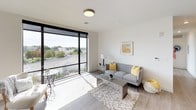 This well-appointed two-bedroom, one-bathroom residence offers a bright, modern living experience across a single floor. The open living area is anchored by floor-to-ceiling windows that frame sweeping outdoor views, flooding the space with natural light and creating an airy, expansive atmosphere. Light wood-style flooring flows throughout, complementing the clean, neutral color palette.

The kitchen features white cabinetry, white appliances including a refrigerator, range, and built-in microwave, and a marble-style countertop that extends into a peninsula with bar seating — ideal for casual dining or entertaining. The layout connects the kitchen seamlessly to the living and dining areas.

Both bedrooms are generously sized and benefit from large windows with urban views, roller shades for privacy, and ample natural light. One bedroom functions well as a home office, complete with a wide window ledge perfect for a desk setup.

The full bathroom offers a dual-sink vanity with a marble-style countertop, dark wood cabinetry, and a large mirror with overhead lighting, providing a clean and functional design. A separate water closet adds additional privacy and convenience. Throughout the unit, the modern design, abundant natural light, and expansive views combine to create a comfortable and stylish living environment.