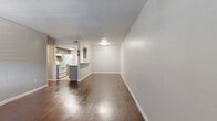 This single-floor, one-bedroom, one-bathroom unit offers a practical and cohesive layout across a compact yet efficient footprint. Rich, dark hardwood flooring flows consistently throughout the living spaces, creating visual warmth and continuity.

The combined living and dining area is the heart of the unit, offering an open, airy feel with neutral white walls, a textured ceiling, and a ceiling-mounted light fixture. A window allows natural light to fill the space. The layout connects seamlessly to the galley-style kitchen, which features gray cabinetry, granite-look countertops, a tile backsplash, a double stainless steel sink, and white appliances including a range and refrigerator. Light tile flooring and under-cabinet lighting complete the kitchen's functional design.

The bedroom is a comfortable size, featuring a ceiling fan with light, a window with blinds for natural light, neutral gray walls, and direct access to a dedicated walk-in closet. The closet is equipped with built-in shelving and hanging rods, providing ample storage.

The bathroom includes a full tub-shower combination with floor-to-ceiling beige tile, a mosaic tile niche, and tile flooring, offering a clean and practical finish. A hallway connects the main living areas to the private spaces, completing the unit's efficient and functional floor plan.