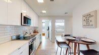 Located at 213 Albany St in Boston's South End neighborhood, this single-floor unit offers a thoughtfully designed layout with a clean, modern aesthetic. The interior is characterized by light hardwood flooring, bright white walls, and recessed lighting that creates a consistently bright and open atmosphere throughout.

The kitchen is a standout feature, showcasing floor-to-ceiling white cabinetry, a white subway tile backsplash, and a full suite of stainless steel appliances including a range, built-in microwave, refrigerator, and dishwasher. A compact dining area with a round table and modern chairs sits adjacent, offering a functional everyday eating space.

Multiple bedrooms are fitted with built-in Murphy beds paired with integrated wardrobe storage and dedicated desk areas. Large windows in the bedrooms provide notable natural light and outward views of the surrounding cityscape, enhancing the sense of space. Each room offers a versatile, efficient layout well-suited for both sleeping and working.

The unit includes two bathrooms. One features warm-toned stone tile flooring, a glass-enclosed walk-in shower, and a white vanity. The second bathroom echoes the same tile flooring and includes a wall-mounted floating vanity with an illuminated mirror, reinforcing the unit's consistent modern design language.
