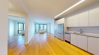 This well-appointed single-floor residence offers a clean, contemporary design defined by crisp white walls, warm honey-toned hardwood flooring, and an abundance of natural light. An entry hallway leads seamlessly into the open living area, where large windows frame urban views and fill the space with daylight.

The kitchen is thoughtfully designed with white cabinetry extending to the ceiling, a classic subway tile backsplash, and a full suite of stainless steel appliances including a range, microwave, dishwasher, and refrigerator. The layout is efficient yet generous, with ample counter and storage space.

The living area is open and airy, with clean sightlines and continuity in the hardwood flooring that enhances the sense of space. Multiple rooms benefit from windows with city views, and select rooms include access to outdoor areas, allowing for fresh air and additional natural light.

The bathroom is finished in neutral grey floor tiles and features a full soaking tub with shower, wall-mounted vanity with an integrated sink, a large mirror, and accessibility grab bars throughout, reflecting a thoughtful and inclusive design approach.

Overall, the residence presents a bright, modern aesthetic with consistent finishes and a functional layout suited to comfortable everyday living.