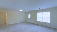 This two-story property offers a clean, functional layout designed to maximize comfort and usability across both levels. The pictured room exemplifies the home's straightforward aesthetic, featuring soft, neutral-toned walls in a warm off-white that create a calm and welcoming atmosphere. The room is finished with wall-to-wall carpeting in a light beige tone, adding warmth underfoot and contributing to an overall sense of comfort. A flush-mount ceiling light fixture provides overhead illumination, complementing the natural light that enters through two windows fitted with white blinds. An exterior-facing door with a window insert offers both access and additional light. The clean white baseboards provide a crisp contrast against the walls, lending a tidy, well-maintained appearance. The room's open layout offers flexibility for a variety of furniture arrangements and uses. The minimalist finishes throughout suggest a move-in-ready space that is easy to personalize. With two floors, the property provides ample room to separate living and private spaces, making it well-suited for a range of occupants seeking a straightforward and practical home environment.
