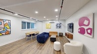 Located at 1701 Federal St in Philadelphia's Graduate Hospital neighborhood, this thoughtfully designed common space offers a versatile and inviting environment across a single level. The open floor plan is anchored by warm hardwood-style flooring and crisp white walls adorned with a rotating collection of vibrant, contemporary artwork that adds color and personality throughout.

The lounge area features plush seating, including a deep navy sofa, a cognac leather bench, and a rounded white armchair, arranged around a coffee table and oriented toward a wall-mounted flat-screen television with a floating walnut media console. A pool table positioned toward the rear of the space adds a recreational focal point, making the room ideal for social gatherings.

A dedicated dining area with a light wood table and seating for several occupants sits near a row of windows that bring in natural light. The kitchenette is well-equipped with dark cabinetry, white upper cabinets, quartz countertops, a herringbone tile backsplash, stainless steel appliances including a full-size refrigerator and dishwasher, and an island with bar seating. Recessed lighting and exposed industrial piping along the ceiling contribute to the space's modern-industrial aesthetic, while a wall-mounted split HVAC unit ensures year-round comfort. Double entry doors provide easy access to and from the space.