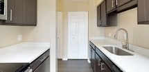 This single-floor high-rise unit offers a thoughtfully arranged layout with a variety of functional spaces and standout architectural features. The most striking element is a glass-enclosed sunroom framed by floor-to-ceiling windows and a fully glazed ceiling, flooding the area with natural light and offering panoramic views of the surrounding cityscape and skyline. Dark hardwood-style flooring runs through this sunroom and connecting living areas, lending a sleek, modern contrast to the warm beige walls throughout.

The living spaces include generously sized carpeted rooms, each receiving abundant natural light through large windows that frame elevated city views. Baseboard heating units line the walls beneath the windows, and textured ceilings add a classic finish throughout much of the unit.

The galley-style kitchen is efficiently designed, featuring dark espresso cabinetry paired with light countertops, a stainless steel sink, and dark hardwood-style flooring. A closet at the end of the kitchen provides additional storage.

The bedrooms are carpeted and well-proportioned, with one featuring access to a walk-in closet area and an additional storage closet. Two bathrooms serve the unit: one includes a soaker tub with a safety bar and a dark-framed vanity mirror over a stone-topped vanity, while the second features a tub-shower combination with sliding glass doors.