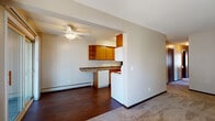 This single-floor residential unit offers a functional and well-organized layout designed for comfortable everyday living. The open-concept living and dining area is finished with durable hardwood-style flooring and features a ceiling fan with light fixture. Baseboard heating is present throughout, ensuring efficient climate control across all rooms.

The kitchen is positioned adjacent to the living area and is equipped with warm oak cabinetry, open upper shelving, dark granite-style countertops, a breakfast bar overhang, a dishwasher, electric range, and a refrigerator. A dedicated entry corridor connects the kitchen to the rest of the unit.

The spacious living room features plush carpeting and a sliding glass door that opens to an outdoor area, allowing natural light to fill the space. Two carpeted bedrooms each include ceiling fans, baseboard heating, and large windows that invite natural light and offer views of the surrounding neighborhood and greenery. One bedroom also includes a wall-mounted air conditioning unit for added comfort.

The bathroom is outfitted with a single-sink vanity with an oak cabinet base, a large wall mirror, tile wainscoting, and a separate tub-shower combination with white square tile surround. The overall aesthetic is clean, neutral, and practical throughout.
