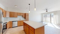 This single-floor, three-bedroom, two-bathroom unit in Baraboo, Wisconsin offers a thoughtfully designed open layout with modern finishes throughout. The kitchen is a standout feature, equipped with warm honey-toned cabinetry, stainless steel appliances—including a refrigerator, range, microwave, and dishwasher—and a large central island with a clean white countertop. Pendant lighting above the island adds a contemporary touch, while light wood-look flooring extends seamlessly into the adjacent living room, which features a ceiling fan and a sliding glass door that floods the space with natural light and provides outdoor views.

The three bedrooms are carpeted for comfort, each featuring neutral white walls and ceiling fans or windows that bring in natural light. The primary bedroom is generously sized and includes a walk-in closet outfitted with wire shelving systems for organized storage.

The primary bathroom features a walk-in shower with a glass door, a wood-toned vanity with a white countertop, and a large mirror with overhead lighting. Light vinyl flooring ties the space together cleanly. The unit's overall aesthetic is modern and neutral, providing a bright, move-in-ready environment.