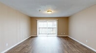 This single-floor unit at 2651 Thomas Lane in Augusta, Georgia offers a practical, well-organized layout across several distinct living spaces. The living room serves as the central gathering area, finished with durable wood-look flooring and warm neutral-toned walls. A large sliding glass door fitted with vertical blinds fills the room with natural light and provides direct access to an outdoor balcony, adding an open, airy quality to the space.

The kitchen is equipped with rich, medium-toned wood cabinetry extending to the upper walls for generous storage, granite-style countertops, a built-in sink, and black appliances including an electric range and refrigerator. Light tile flooring runs throughout the kitchen area, which opens conveniently toward the living room.

The bedrooms feature the same wood-look flooring found in the living areas, with neutral walls and windows providing natural light. One bedroom includes a dedicated walk-in closet outfitted with dual hanging rods and shelving along multiple walls, offering substantial storage capacity. Additional closet access is available in the bedroom corridor.

The bathroom includes a tiled tub-shower combination, a toilet, and a vanity with wood cabinetry, a dark countertop, and a wall-mounted mirror. Light tile flooring completes the bathroom. Textured ceilings are consistent throughout the unit.