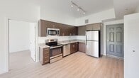 This contemporary single-floor residence offers a well-designed open-concept layout that seamlessly connects the kitchen and living areas. The kitchen is a standout feature, outfitted with dark-toned wood cabinetry, granite countertops, a subway tile backsplash, and a full suite of stainless steel appliances including a range, microwave, dishwasher, and refrigerator. Track lighting overhead highlights the clean lines and modern finishes throughout. Light hardwood-style flooring runs through the main living areas, enhancing the bright and airy atmosphere created by soaring ceilings and abundant natural light. The living area opens to the outdoors through sliding glass doors, offering views of a lush green lawn and surrounding landscaping. A ceiling fan adds a functional touch to the living space. The unit includes two well-appointed bathrooms, each featuring granite-topped dark wood vanities, large-format tile flooring, and full soaking tubs with tiled surrounds. A dedicated bedroom benefits from a large window framing tranquil greenspace views and is finished with the same light wood flooring. Throughout the unit, crisp white walls and consistent, high-quality finishes create a cohesive modern aesthetic that is both practical and inviting.
