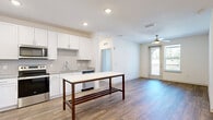 This single-floor residence offers a clean, modern design highlighted by an open-concept layout connecting the kitchen and living area. The kitchen is well-appointed with white shaker cabinetry, gray subway tile backsplash, granite-look countertops, and a full suite of stainless steel appliances, including a refrigerator, range, microwave, and dishwasher. A freestanding kitchen island with a white top and dark wood frame provides additional prep and dining space. Recessed lighting and wood-look plank flooring carry throughout the main living areas, which also feature a ceiling fan and access to an outdoor balcony.

The bedrooms are carpeted and naturally lit by windows with blinds, each equipped with ceiling fans. The primary bedroom connects to a private bathroom featuring a granite-topped vanity, a large framed mirror, a marble-tiled walk-in shower, and an adjacent walk-in closet with wire shelving. A dedicated laundry area houses a full-size top-load washer and dryer with overhead wire shelving for added storage. Additional rooms offer hardwood-style flooring and bright, neutral walls, lending the overall space a clean, move-in-ready aesthetic.