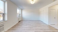 Located at 29-31 Upper Canada Dr, Unit 204, in Toronto's desirable North York neighbourhood, this thoughtfully designed unit offers a clean, modern aesthetic across a well-utilized single floor. The interior is finished with light grey laminate hardwood flooring throughout the living areas, complemented by crisp white walls that enhance the sense of brightness and openness.

The space includes two living areas, providing flexibility for both lounging and dining or workspace arrangements. Each room benefits from large windows with views of surrounding greenery, allowing generous natural light to fill the interiors. Traditional radiator heating units are present in each room, adding a classic functional element.

The kitchen area features a built-in desk or breakfast counter nook with overhead cabinetry, finished in white with gold-toned hardware, alongside light tile flooring that transitions seamlessly from the main living spaces.

Both bathrooms are finished to a high standard, with one featuring a full soaking tub framed by elegant marble-effect porcelain wall tiles in white and grey tones, paired with polished chrome fixtures. A hallway connects the key areas of the unit, contributing to a practical and efficient layout. The overall ambiance is clean, airy, and move-in ready, well-suited for comfortable urban living in Toronto.