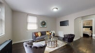 This well-appointed single-floor residence offers a thoughtfully designed layout that balances comfort and modern style. The living room serves as the heart of the space, featuring rich dark hardwood flooring, neutral warm-toned walls, and multiple windows fitted with blinds that allow for controlled natural light. A cast-iron radiator adds a classic architectural touch, complementing the room's contemporary furnishings and arched entryway detail.

The kitchen is bright and functional, outfitted with crisp white shaker cabinetry, light wood-tone flooring, and a full suite of stainless steel appliances including a gas range, over-the-range microwave, and refrigerator. A peninsula provides additional counter space and a natural transition into the adjacent dining area, which comfortably accommodates a small dining set.

The bedroom is serene and well-proportioned, with the same dark hardwood flooring found throughout the living areas. It includes a dedicated closet and is connected to a hallway that also features an additional storage closet.

The bathroom is finished with marble-look wall tile surrounding the soaking tub and shower, a window for natural ventilation, and a classic cast-iron radiator that echoes the vintage character found elsewhere in the space. Clean white fixtures complete the polished look.