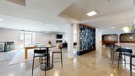 Located at 127 N 17th St in Richmond, VA, this expansive single-floor amenity space offers a thoughtfully designed, open-plan layout that blends contemporary style with a welcoming, social atmosphere. Polished concrete floors extend throughout, reflecting natural light that pours in through large windows, enhancing the bright and airy feel of the space.

The layout is cleverly zoned using a striking floor-to-ceiling open-grid bookshelf divider with a warm wood frame, which separates the lounge area from the games zone without closing off the open-plan feel. The lounge area features a linear gas fireplace, a wall-mounted TV, and comfortable seating, creating an inviting gathering spot. A pair of ping-pong and billiards tables anchor the central games area, complemented by high-top bar tables and stools positioned throughout.

Along one wall, a fully equipped kitchen showcases bold navy-blue tile backsplash extending to the ceiling, white shaker cabinetry, granite countertops, stainless steel appliances including a dishwasher and refrigerator, and a generous island with counter seating. Tucked into arched navy alcoves are intimate banquette-style booths, adding a distinctive and cozy contrast to the otherwise open environment. Exposed industrial ductwork overhead adds a loft-like character, tying together the modern and industrial design elements throughout this versatile communal space.