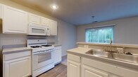 Located at 6345 Cooper Rd in Columbus, Ohio, this two-story home offers a well-organized layout designed for comfortable everyday living. The kitchen is a functional centerpiece, featuring white cabinetry with raised-panel doors, a gas range, over-the-range microwave, refrigerator, and a peninsula with a stainless steel sink. Wood-look flooring runs through the kitchen, which flows naturally into the adjacent living and dining area. The living space is generously proportioned, with soaring ceilings, plush wall-to-wall carpeting, a sliding glass door leading to the outdoors, and a large picture window that fills the room with natural light. A conveniently located half bathroom on the main level serves guests. Upstairs, the carpeted bedrooms offer a quiet retreat, each with windows that bring in ample daylight. The upper-level bathrooms are clean and well-appointed — one features a tub-shower combination, while another includes a walk-in shower — both with white vanities and wood-look flooring. A staircase connects the two floors, as visible in the spatial overview. Throughout the home, a neutral color palette of warm beige and soft white tones creates a cohesive, move-in-ready atmosphere.
