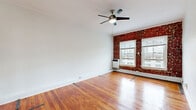 This well-appointed one-bedroom, one-bathroom residence offers a thoughtfully designed single-floor layout that makes excellent use of its space. Rich, warm-toned hardwood floors run continuously throughout, lending a sense of cohesion and character to every room.

The living room serves as a welcoming centerpiece, showcasing a striking exposed brick accent wall framing multiple windows that invite natural light. A ceiling fan overhead adds both style and practicality to the space.

The kitchen is efficiently configured with a clean galley-style layout. White shaker cabinetry lines the walls, paired with light countertops, a stainless steel sink, and a range with a ventilation hood — providing all the essentials in a tidy, functional arrangement.

The bedroom continues the home's warm aesthetic, featuring the same beautiful hardwood floors, an exposed brick wall with a window offering natural light, and a double-door closet for ample storage.

Two hallways connect the rooms with a smooth flow, highlighted by an elegant arched doorway that adds a classic architectural touch. Crown molding accents the ceilings throughout, reinforcing the home's timeless character.

The bathroom is finished in crisp white tile, complete with a full soaking tub, vanity with sink, and a bright window for natural ventilation.