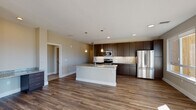 This single-floor residence features a contemporary open-concept design that seamlessly integrates the kitchen and living areas. The kitchen is a standout space, outfitted with rich dark espresso cabinetry extending to the ceiling, granite countertops, a white subway tile backsplash, and stainless steel appliances including a range, microwave, and full-size refrigerator. A central island with a granite surface and pendant lighting above provides additional prep space and casual seating.

The living area is bathed in natural light through large windows and a glass door that open to an outdoor balcony, offering expansive mountain views. Durable wood-style flooring runs throughout the main living spaces, complementing the neutral warm-gray walls.

The primary bathroom includes a walk-in glass shower with tile surround, dark vanity cabinetry, and granite countertops. A second full bathroom features a tub-shower combo with the same consistent cabinetry and granite finishes. The carpeted bedroom benefits from a ceiling fan and a generous window framing scenic mountain views.

A dedicated laundry room houses a full-size washer and dryer with dark upper cabinetry for additional storage, completing this well-appointed residence.