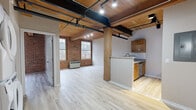 Located at 101 Whiting St in Winsted, CT, this two-bedroom, one-bathroom loft-style residence masterfully blends industrial character with contemporary updates. The open-concept living and kitchen area immediately impresses with its exposed wood-plank ceiling, black steel support beams, and track lighting that together create a warm yet urban aesthetic. Original exposed brick walls add rich texture and historic charm, while large multi-pane windows flood the space with natural light and offer views of the surrounding wooded landscape.

The kitchen features warm-toned wood cabinetry, granite countertops, a subway tile backsplash, and stainless steel appliances, including a refrigerator, electric range, and dishwasher. A peninsula counter opens the kitchen to the living area, enhancing the open-plan feel.

Both bedrooms offer light wood-tone flooring, neutral walls, and closet storage, with the primary bedroom benefiting from generous proportions and a walk-in closet with built-in shelving. The bathroom is finished with a stylish wood-paneled vanity, white countertop, modern matte black fixtures, and a mirrored medicine cabinet. A dedicated laundry area completes the practical layout of this well-appointed industrial loft.