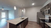 Located at 5072 Timberhill Dr in Leon Valley, TX, this single-floor residence offers a thoughtfully designed open-concept layout with contemporary finishes throughout. The kitchen serves as a central highlight, featuring a large island with granite countertops, an undermount sink, dark espresso cabinetry, and a full suite of stainless steel appliances including a refrigerator, range, microwave, and dishwasher. Elegant pendant lighting hangs above the island, adding a modern touch. A tile backsplash adds visual interest behind the range area. Wood-style plank flooring runs throughout the main living areas, seamlessly connecting the kitchen to the open living room, which is equipped with a ceiling fan. The bedrooms are carpeted for comfort, feature ceiling fans, and benefit from natural light through standard and transom windows. The bathroom is well-appointed with granite countertops on dark cabinetry, wood-style flooring, a large framed mirror, and a full tub and shower combination surrounded by classic white subway tile. A separate walk-in shower with patterned tile flooring is also present. Double entry closet doors and generous storage round out this clean, modern residence.