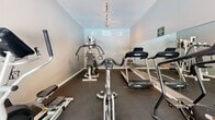 This fitness center, located in Concord, CA (94518), is a dedicated single-floor workout facility designed to support a comprehensive exercise routine. The space features dark rubber flooring throughout, providing a durable, slip-resistant surface ideal for high-intensity training. Mirrored walls line one side of the room, visually expanding the space and allowing users to monitor their form during workouts.

The cardio section is well-appointed with multiple treadmills, a stationary spin bike, and an elliptical trainer, catering to a variety of aerobic workout preferences. A multi-station strength training machine and free weights round out the strength training options available within the space. Stability balls are also present for core and flexibility exercises.

Natural light fills the room through a set of elegant French doors that open directly to an outdoor pool area, offering pleasant views and a bright, motivating atmosphere. A wall-mounted flat-screen television is positioned above the French doors, providing entertainment during workouts. Overhead track lighting ensures the space is well-lit at all times. Ventilation is supported by multiple ceiling vents. Signage indicates the space is reserved for adult residents only, reinforcing its community amenity status.