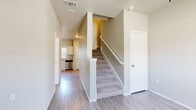This two-story residence offers a thoughtfully designed layout with a clean, neutral palette that creates a bright and welcoming atmosphere throughout. The main level features light wood-look flooring that flows through the entryway and into the kitchen, where white raised-panel cabinetry pairs with granite-look countertops and a full suite of stainless steel appliances, including a refrigerator, range, microwave, and dishwasher. A window above the sink allows natural light to fill the space. The staircase, finished with carpet treads and white railings, connects the two levels and serves as a central architectural element on the main floor. The upper level houses carpeted bedrooms, each offering a quiet, comfortable retreat. One bedroom features double louvered closet doors and a window with blinds for natural light and privacy. The bathrooms are well-appointed, with one featuring a white vanity topped with a bold, patterned granite countertop and a large mirror, while another includes a full soaking tub with a tile surround and chrome fixtures. Throughout the home, consistent neutral wall tones and clean white trim contribute to a cohesive and move-in-ready aesthetic.