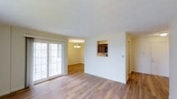 This single-floor residence offers a well-connected, open layout that seamlessly integrates the living, dining, and kitchen areas. The living space is finished with warm hardwood-style flooring that extends throughout, creating a cohesive and inviting atmosphere. Large sliding glass doors flood the room with natural light while providing access to an outdoor area, enhancing the sense of openness and connectivity with the exterior.

Adjacent to the living area, the dining space is highlighted by a tasteful chandelier that adds a refined touch to everyday gatherings. A pass-through window connects the dining area to the kitchen, offering both functional convenience and a glimpse of the dark wood cabinetry within. The kitchen features rich, dark-toned cabinets that contrast elegantly against the lighter walls and flooring.

Throughout the space, neutral wall tones and a textured ceiling contribute to a clean, understated aesthetic. The layout is practical and efficient, making excellent use of the available footprint while maintaining a comfortable flow between areas. Overall, this residence combines functional design with warm finishes to create a welcoming, livable environment suited to a variety of lifestyles.