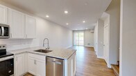 Located at 440 W 14 Mile Rd in Clawson, Michigan, this two-bedroom, two-bathroom residence spans two floors, offering a well-organized and functional layout. The main floor hosts the combined kitchen and living area, where light hardwood flooring flows throughout, creating a bright and cohesive atmosphere. The kitchen is outfitted with white shaker-style cabinetry, granite countertops, a subway tile backsplash, stainless steel appliances including a refrigerator, range, and microwave, and a peninsula with a built-in sink — ideal for both cooking and casual dining. The living area features recessed lighting and a sliding glass door that opens to an outdoor balcony, filling the room with natural light and outdoor views. Both bathrooms continue the granite countertop theme with white vanity cabinetry; one includes a tub-shower combo, while the other features a walk-in shower with built-in shelving niches. The spacious primary bedroom is complemented by a well-appointed walk-in closet with built-in shelving and hanging rods. The second floor provides additional bedroom space, each room featuring clean neutral walls and consistent hardwood flooring. A dedicated staircase connects the two levels, and two closets provide ample storage throughout.