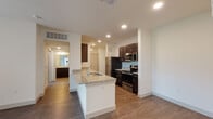 This single-floor residence is thoughtfully designed with a contemporary aesthetic and a practical open-concept layout. The kitchen serves as the heart of the space, featuring rich dark-espresso cabinetry paired with light granite countertops that extend across both the perimeter surfaces and a central island with an integrated sink. Stainless steel appliances — including a refrigerator, electric range, microwave, and dishwasher — complete the well-equipped culinary space. Wood-style plank flooring runs throughout the kitchen and living areas, adding warmth and visual continuity.

The living area flows seamlessly from the kitchen, offering an open and airy feel enhanced by recessed lighting and clean white walls. A hallway connects the main living space to the bedrooms, each finished with plush carpeting, ceiling fans, and windows that invite natural light and outdoor views of surrounding greenery.

The bathrooms maintain the same design language as the kitchen, with matching dark cabinetry and granite countertops. The primary bathroom features a dual-sink vanity with a large mirror and a tiled walk-in shower, while a secondary bathroom offers a single-sink vanity. Throughout the unit, a consistent, modern palette creates a cohesive and polished ambiance.