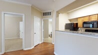 This single-story residence showcases a well-considered layout connecting its primary living areas through a central hallway finished with rich hardwood flooring and crisp white trim. Crown molding runs consistently throughout the home, lending a polished architectural detail to each room.

The living area is bright and open, benefiting from a ceiling fan with light fixture and a set of French doors that invite natural light and provide access to an outdoor patio. The kitchen is efficiently laid out with warm wood cabinetry, granite-look countertops, and a full suite of black appliances, including an electric range, over-the-range microwave, and dishwasher. A pass-through counter connects the kitchen to the adjacent area, enhancing the open feel. A utility closet is accessible directly from the kitchen.

The bedroom features plush carpeting, crown molding, and a distinctive angled bay window that frames natural light from multiple directions. A ceiling fan adds comfort to this generously proportioned room.

The bathroom is finished with tile flooring, a wide vanity topped with granite-style counters, warm wood cabinetry, a large mirror, and a shower-tub combination. The overall palette of soft beige tones throughout creates a cohesive and calm ambiance.