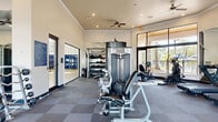 Located at 3701 Grandewood Blvd in Orlando, Florida, this fitness center offers a generously sized, single-floor workout facility designed to accommodate a comprehensive range of exercise routines. The space is thoughtfully laid out across a wide, open floor plan finished with durable, cushioned tile flooring in a checkered pattern ideal for high-traffic athletic use.

The facility is outfitted with an impressive selection of equipment, including cable weight machines, a squat rack with bench press, a multi-station strength machine, treadmills, a stationary bike, and a full rack of dumbbells spanning a wide weight range. Floor-to-ceiling mirrors line portions of the walls, enhancing the sense of openness and allowing users to monitor their form during workouts.

Natural light fills the space through large, multi-pane windows and glass doors that frame views of lush outdoor greenery and a surrounding patio area. Recessed lighting and multiple ceiling fans throughout ensure consistent illumination and airflow. Crown molding and tray ceiling details in select areas add a polished, refined touch to the interior.

The overall ambiance is clean, bright, and motivating — combining practical fitness functionality with an inviting atmosphere suited for daily use.