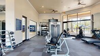 Located at 3701 Grandewood Blvd in Orlando, Florida, this fitness center offers a generously sized, single-floor workout facility designed to accommodate a comprehensive range of exercise routines. The space is thoughtfully laid out across a wide, open floor plan finished with durable, cushioned tile flooring in a checkered pattern ideal for high-traffic athletic use.

The facility is outfitted with an impressive selection of equipment, including cable weight machines, a squat rack with bench press, a multi-station strength machine, treadmills, a stationary bike, and a full rack of dumbbells spanning a wide weight range. Floor-to-ceiling mirrors line portions of the walls, enhancing the sense of openness and allowing users to monitor their form during workouts.

Natural light fills the space through large, multi-pane windows and glass doors that frame views of lush outdoor greenery and a surrounding patio area. Recessed lighting and multiple ceiling fans throughout ensure consistent illumination and airflow. Crown molding and tray ceiling details in select areas add a polished, refined touch to the interior.

The overall ambiance is clean, bright, and motivating — combining practical fitness functionality with an inviting atmosphere suited for daily use.