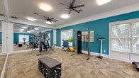 Located at 100 Ivey Park Lane in Norcross, Georgia, this well-equipped fitness center offers a comprehensive workout environment designed to support a wide range of exercise routines. The space is defined by bold teal accent walls, crisp white crown molding, and neutral patterned carpet flooring that together create an energetic yet clean aesthetic.

The facility is divided into two connected workout zones. The strength and functional training area is stocked with a multi-station cable machine, adjustable weight bench, a rack of kettlebells, medicine balls, resistance bands, stability balls, and a balance board — providing ample options for both resistance and functional training. Full-length mirrors line one entire wall, visually expanding the space and allowing users to monitor their form during exercise. Dual ceiling fans overhead ensure consistent air circulation throughout.

The adjacent cardio zone features a treadmill, elliptical, and stationary bike, all positioned beneath another ceiling fan and alongside large windows that invite generous natural light and views of the surrounding greenery. The windows, fitted with blinds throughout, allow for flexible light control. Together, both areas form a cohesive, well-lit fitness facility that accommodates cardio, strength, and functional training needs in a comfortable, inviting environment.
