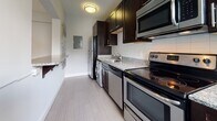 Located at 200 Rhode Island Avenue NE in Washington, DC, this single-floor unit offers a clean, modern aesthetic throughout its well-appointed layout. Warm hardwood flooring flows continuously through the main living areas, complementing the cool gray-toned walls and crisp white trim and doors that define the interior design.

The living area is bathed in natural light, courtesy of a set of large windows flanking a glass-paneled exterior door fitted with slatted blinds. A wall-mounted mini-split unit provides efficient climate control, keeping the space comfortable year-round. The open feel of the room is enhanced by its generous proportions and unobstructed sightlines.

The kitchen is efficiently designed with a galley-style layout, featuring rich dark espresso cabinetry, granite countertops, white subway tile backsplash, and a full suite of stainless steel appliances including a refrigerator, electric range, microwave, and dishwasher. An in-unit washer is also integrated into the kitchen space, adding everyday convenience.

The bathroom is bright and clean, finished with large-format light gray floor tiles, white walls, and a natural light source from a window with blinds. The entryway provides a welcoming transition into the unit, featuring the same hardwood flooring and a solid, well-framed front door. Overall, the space presents a practical yet polished environment suited for comfortable urban living in Washington, DC.