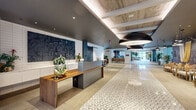 Located at 101 Washington Street in Conshohocken, PA, this expansive single-floor amenity space offers nearly 7,700 square feet of thoughtfully designed, upscale communal areas. The grand entry lobby sets an immediate tone with its geometric patterned tile flooring, a sleek reception desk with warm wood accents, bold oversized pendant lighting, and a corridor that draws the eye toward abundant natural light at the far end.

The space transitions into a dramatic double-height great room anchored by floor-to-ceiling steel-framed windows that frame lush outdoor greenery. Soaring wood-paneled ceilings, exposed stone accent walls, and large indoor trees create a biophilic atmosphere throughout. A sunken lounge area with built-in seating and curated artwork adds an inviting, layered dimension to the layout.

A dedicated game lounge features a full-size pool table surrounded by comfortable seating, benefiting from the same sweeping glazed walls and natural light. The full demonstration kitchen includes a long island with patterned tile paneling, bar seating, industrial pendant lighting, open shelving, and adjacent dining tables — ideal for social gatherings. A glass-enclosed private meeting or lounge room with chevron-patterned wall treatments offers a more intimate setting. An upper-level mezzanine with slatted wood detailing and wire-rail balustrades overlooks the main floor, completing this refined, modern amenity destination.