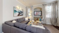 This single-floor residence offers a thoughtfully designed layout with a cohesive neutral palette and wood-look flooring that flows throughout the main living areas. The dining area is anchored by a charming bay window configuration that allows abundant natural light to fill the space, complemented by crown molding and a pendant light fixture overhead. The living room is generously sized, featuring crown molding, a built-in arched media niche, and large windows dressed with elegant floor-to-ceiling drapes. The kitchen is outfitted with stainless steel appliances, warm wood-toned cabinetry, a mosaic tile backsplash, and light quartz countertops with an extended breakfast bar. Both bedrooms are carpeted and well-proportioned, each offering sliding glass door access to the outdoors and ample room for full furniture arrangements. The primary bedroom connects to a spacious walk-in closet equipped with extensive wire shelving and hanging systems for optimized storage. Two full bathrooms serve the residence, each featuring wood-look flooring, a soaking tub with shower, modern vanity cabinetry, and white countertops. Together, these elements create a comfortable and functional living environment with a clean, contemporary aesthetic.
